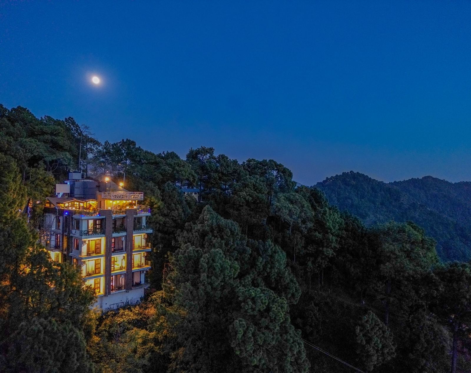 A drone shot of DLS Whispering Winds, Kasauli, surrounded by tress, mountains and lush greenery.